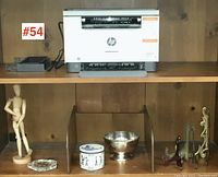 Shelf displaying assorted decorative items including wooden mannequin, glass dish, decorative tin, silver bowl, and metal hooks with HP LaserJet printer above.