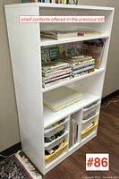 Front view of the white shelving unit showing multiple shelves and plastic storage drawers at the bottom.
