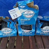 Three new bicycle tires in blue Bikeway by Kenda cardboard packaging. Packaging shows some crushing damage. Tires sized 27.5 x 2.35 mountain bike tires.