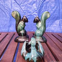 Pair of green and black glazed ceramic squirrel bookends and swan figurine arranged on wooden slats with blue backdrop.