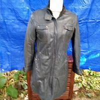 Front view of the long grey leather jacket on a mannequin against a blue tarp background