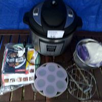 Large Instant Pot Lux Series electric pressure cooker on a wooden surface with manuals and accessories around it.