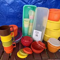 Photo showing colorful stack of Tupperware cups with handles, round containers with lids, tall slender containers and flat storage containers arranged on a table.