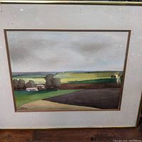 Framed watercolor painting showing a rural landscape with farm buildings and trees in green, brown, and ochre tones under a light cloudy sky.