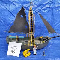 Photo of the full pirate ship with black sails, yellow mast, queen figurine, yellow treasure chest, and anchor.