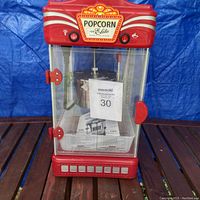 Front view of the red Cuisinart Elite popcorn machine, showing clear glass enclosure, control buttons, and manual inside.