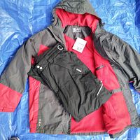Adult snow suit laid open showing gray and red jacket with red fleece interior and black snow pants folded inside the jacket
