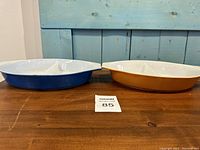 Side view of two Pyrex divided baking dishes on wooden surface, one blue and one orange.
