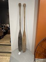 Two full-length wooden paddles leaning against a wall