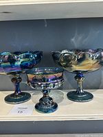 Blue carnival glass trio on shelf showing two scalloped-edged fruit or compote bowls and one goblet with beaded decorative patterns.