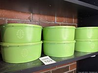 Six green Tupperware containers and lids stacked on a shelf showing the side view with embossed pattern.