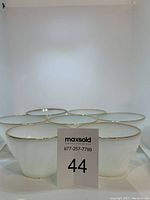 Seven white opaque glass tea cups with gold rims, no handles visible, arranged in a group.