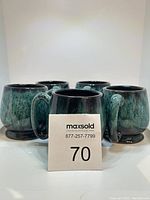 Front angle view of five blue-green pottery mugs grouped together, showing handles and glaze finish.