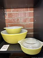 Set of three yellow Pyrex glass items on shelf including two mixing bowls and one covered casserole dish with glass lid.
