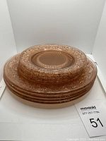 Stack of four pink depression glass dinner plates with detailed embossed floral and geometric patterns.