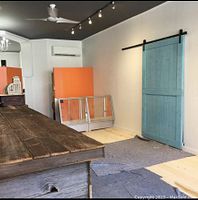 Blue sliding barn door mounted on black metal hardware against a white wall in a room with a wooden table and air conditioning unit.
