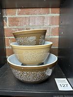 Three vintage Pyrex nesting mixing/serving bowls stacked together showing brown exterior with white Woodland floral pattern and white interior.
