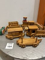 Overall view of the wooden toy train set showing several connected cars, a wooden locomotive, and a small striped pull toy with colored wheels. Some pieces show signs of missing parts or breaks.