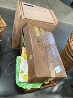 Two cardboard boxes stacked on top of a wicker hamper, one box closed with writing and the other partially open revealing floral fabric pieces