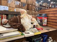 Wide view showing dolls, soldering kits, books lying flat, vintage aluminum shipping box, and wooden cutting board.