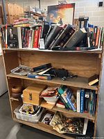 Full view of wooden bookshelf containing mixed items: books, wooden lock box, bowls with snacks, basket with items, vintage camera body, and miscellaneous small objects.