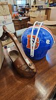 Wooden shoe-shaped item with handle and Denver Broncos football helmet picnic set on a table in warehouse environment.
