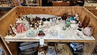 Wide view of collection showing ceramic figurines, brass decor, teacups, mini oil lamps, and various small dishes on a shelf.