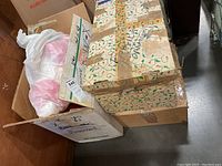 Three closed boxes with holiday wrapping paper and handwritten labels indicating Christmas ornaments inside.