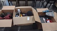 Three open cardboard boxes filled with assorted collectibles including hats and other items