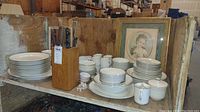 Wide shot showing over 50 pieces of stacked Pope-Gosser china, mostly white ironstone with gold edging, along with a wooden knife block and a dozen cutters.