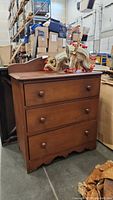 Front right angle view of small wooden dresser with three drawers and elephant purse on top