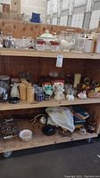 Three shelves of assorted glassware, ceramics, drinkware, collectibles visible including bowls, canisters, ashtrays, and decorative items.