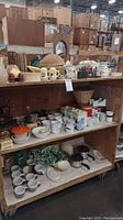 Wide shot showing various mugs, canisters, pottery, vases, cookware, and kitchen items arranged on wooden shelves.