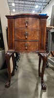 Front view of wooden side table showing three curved drawers with metal ring pulls and carved legs.