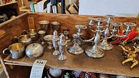 Overview of silver items on shelf including cups, goblets, shakers, candelabras, and short holders.