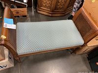 Full view of upholstered bench showing wooden frame, cushion seat, and woven cane panel sides