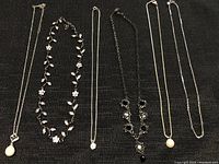 Six fashion necklaces laid out on textured black fabric background, showing detail and variety of styles
