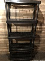 Front view of black resin storage shelf showing four shelves and structure.