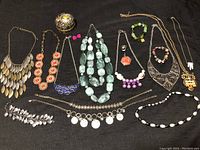 Overview photo of the jewelry lot on black background showing various necklaces, bracelets, and decorative holder