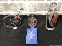 Three decorative perfume bottles shown on a black surface in front of a stone background with a paper tag in front.