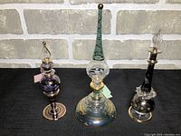 Set of three unique dainty perfume bottles shown together against grey brick background