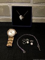 Full view showing all items in the set including necklace in box, watch, bracelet, and earrings arranged on a black surface.