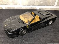Black Ferrari Testarossa convertible scale model viewed from front left angle showing details of the hood, windshield and tan interior seats.