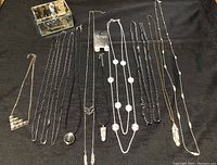 Photo showing assortment of necklaces arranged side by side and the glass jewelry box in the upper left corner containing smaller jewelry items.