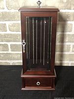 Front view of the wood and glass jewelry box showing the glass door with hanging chains inside.