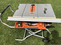 Front view of table saw mounted on stand with integrated wheels, showing aluminum top and fence rail