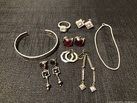 Overview of all silver jewelry items arranged on a dark textured cloth including rings, earrings, bracelets, and necklace.