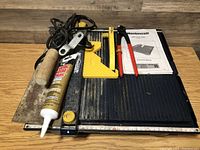 Mastercraft tile saw with tools arranged on top including putty knife, adhesive tube, tile cutter, and manual