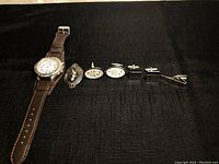 Overview of the men's watch, pin, sterling silver cuff links, and tie clip arranged on a black fabric background.