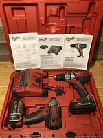 Open red case showing drill, impact driver, charger, batteries, and manuals